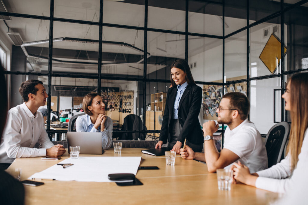 Businesswoman standing and presenting to colleagues seated around a conference table