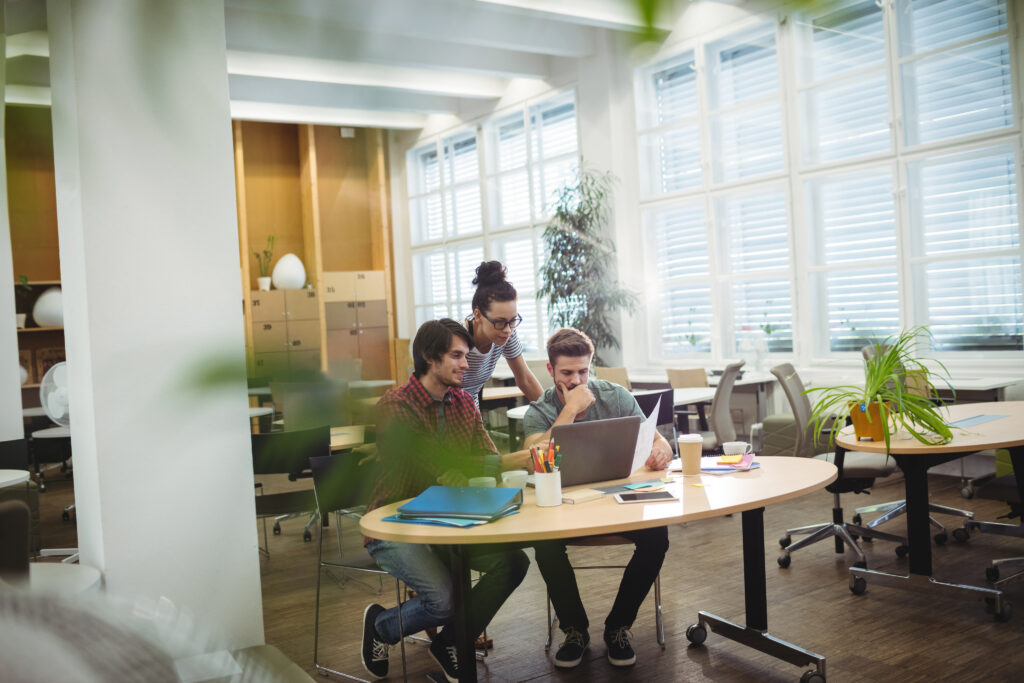 Colleague showing something on a laptop to two seated coworkers in a bright office
