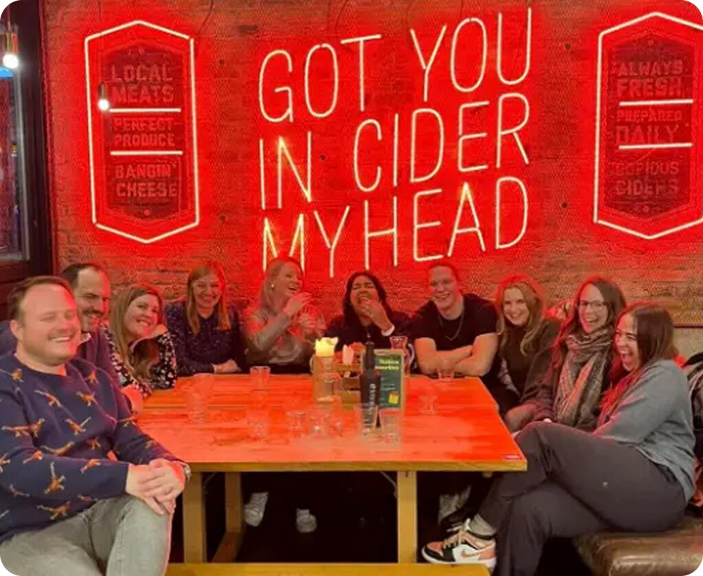 Group of colleagues laughing together at a table under a neon sign