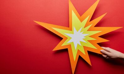 Colorful paper star burst shape on a red background with a hand pointing at it